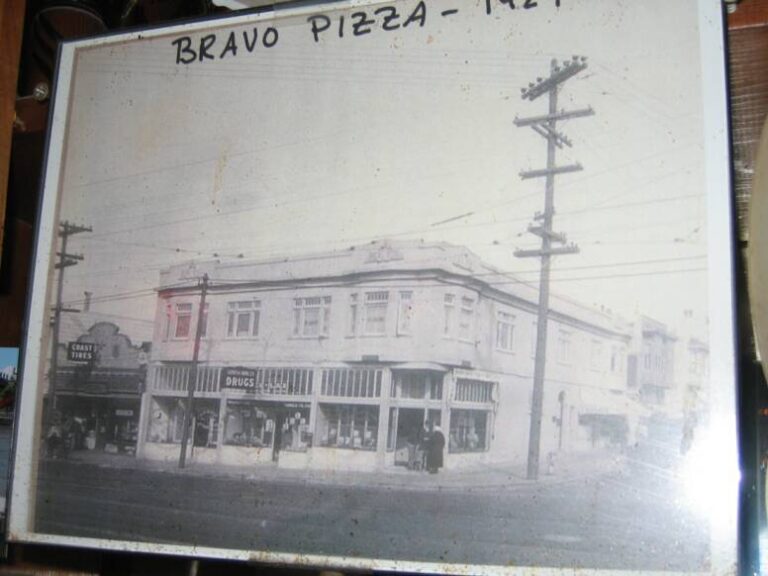 Framed vintage photo of the corner building, hand-labeled Bravo Pizza 1924